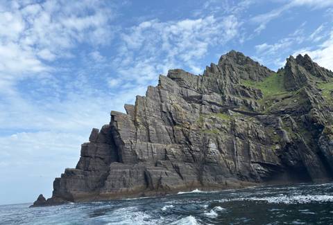      A rocky cliff face with lush greenery under a clear sky.
  