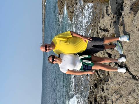       Two people posing by the sea, one in a yellow shirt and the other in a white shirt.
  