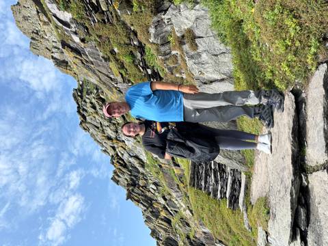      Two people posing on stone steps with a rocky landscape behind.
  