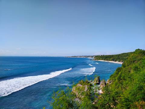 Aerial view of a coastline with waves and green hills.