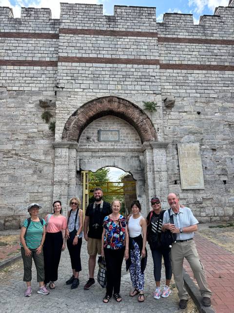 Group of tourists in front of an ancient stone archway.