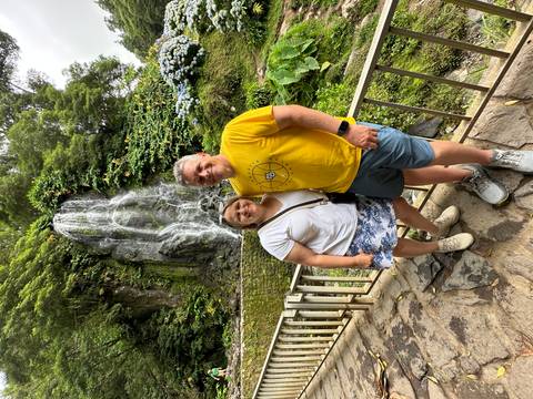 Two people posing in front of a waterfall with lush vegetation.