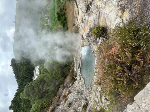 Steaming geothermal pool surrounded by vegetation and hills.