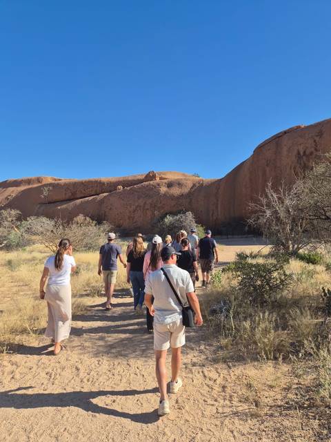       Group of people walking towards a rock formation in the desert.
  