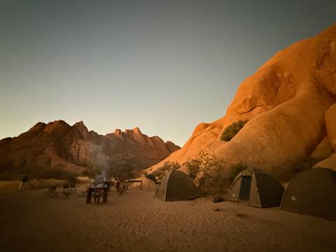 Camping site at dusk with tents and rock formations.