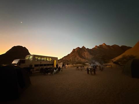 Camping site with a large safari truck and rock formations at sunset.