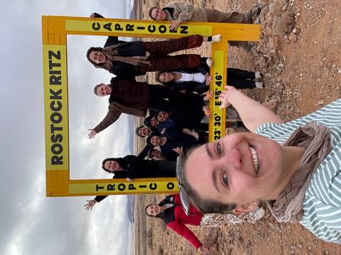 Group posing with a Tropic of Capricorn signboard in a desert.