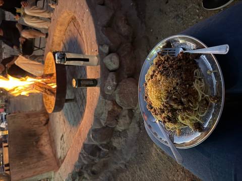 Plate of spaghetti with meat sauce near a campfire.