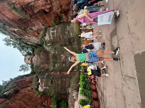 A woman posing in front of the Leshan Giant Buddha with other tourists around.
