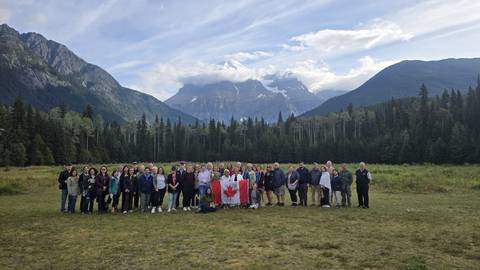 Large group photo in front of mountainous landscape with a Canadian flag.