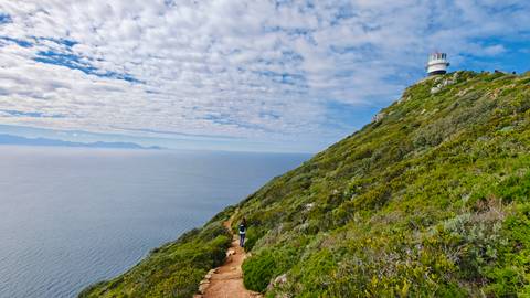 A scenic view of a lighthouse on a hill overlooking the ocean.