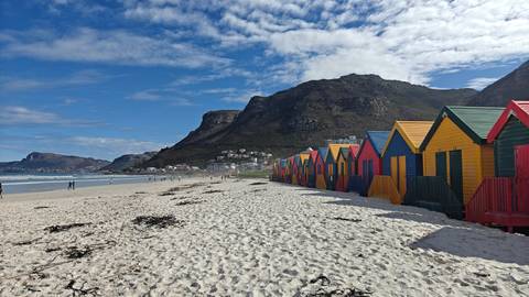 Colorful beach huts along a shoreline with mountains in the background.
