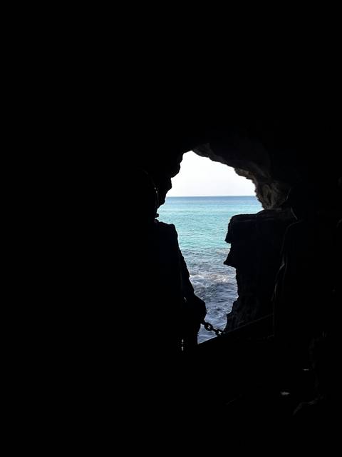       Silhouette of people at a cave entrance overlooking the sea.
  