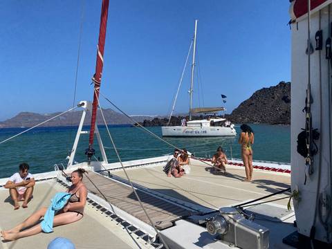 People relaxing on a catamaran with another boat in the background.