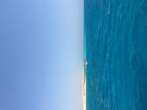       Vast blue sea with a small white boat and distant land.
  