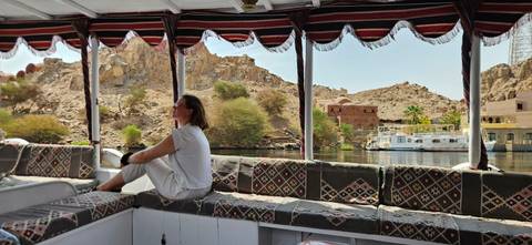       Person relaxing on a boat with scenic background of rocks and vegetation.
  