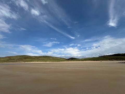 Wide sandy beach with rolling hills and a blue sky.