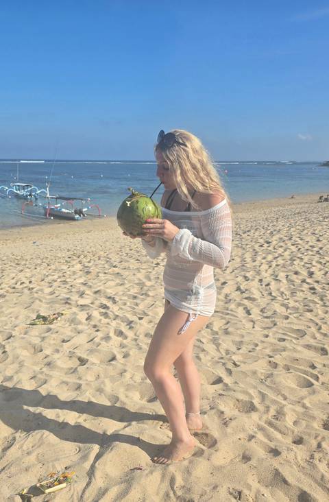 Person sipping from a coconut on a sandy beach.