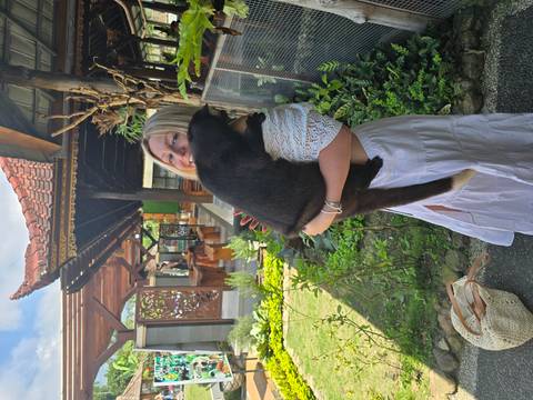 Woman holding a black animal outside a traditional building.