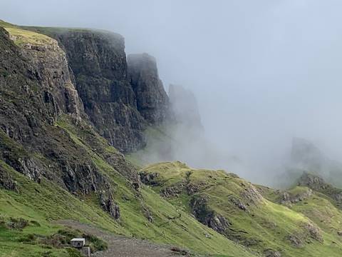       Misty view of steep cliffs and green hills.
  