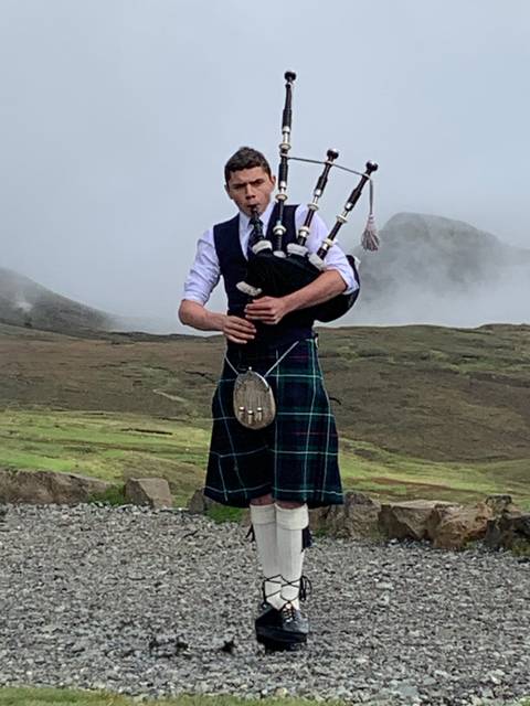 Man playing bagpipes in traditional Scottish attire.