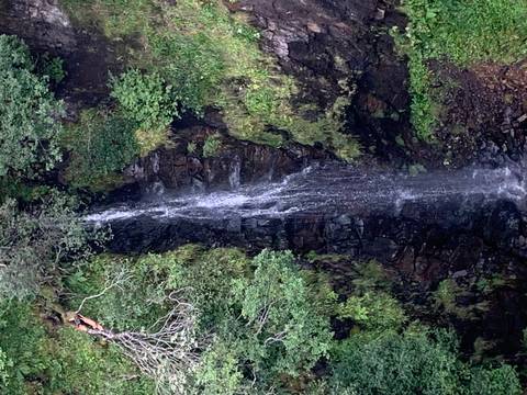 A thin waterfall cascading down a rocky cliffside surrounded by greenery.