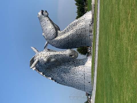       Large horse head sculptures known as The Kelpies situated in a park.
  