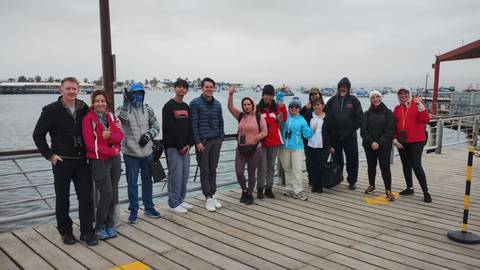       A group of tourists standing on a wooden dock by the harbor.
  