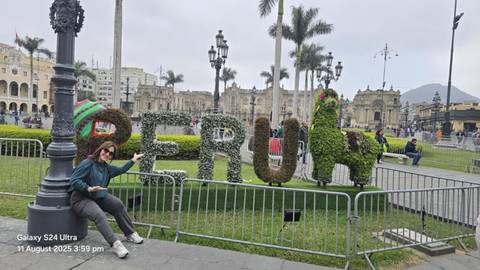       A woman posing with a PERU sign made of plants.
  