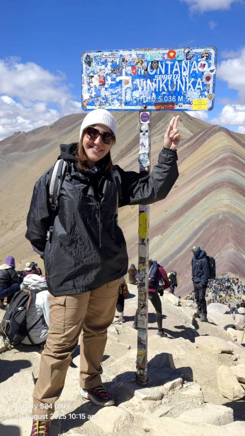       A woman posing next to the colorful Rainbow Mountain.
  