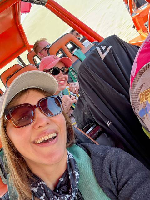       Group of people smiling inside a vehicle, wearing hats and sunglasses.
  