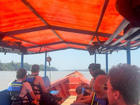       Group of people on a boat in a river with an orange canopy.
  