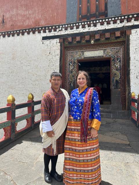 Two people in traditional Bhutanese dress posing in front of a temple.