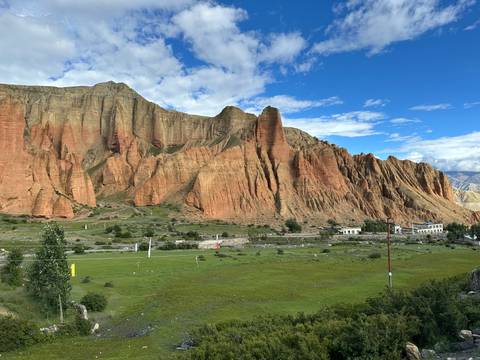       Rocky cliffs with green fields and small structures.
  