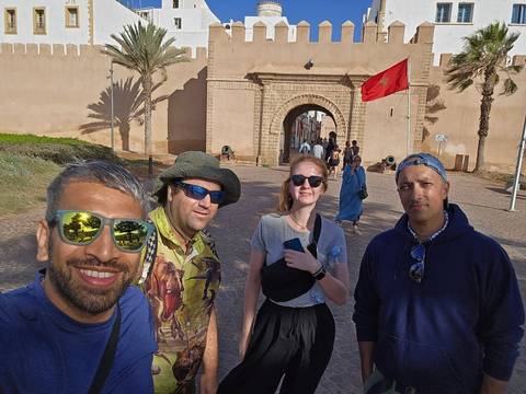       Group of tourists taking a selfie at a historic gate with a Moroccan flag.
  