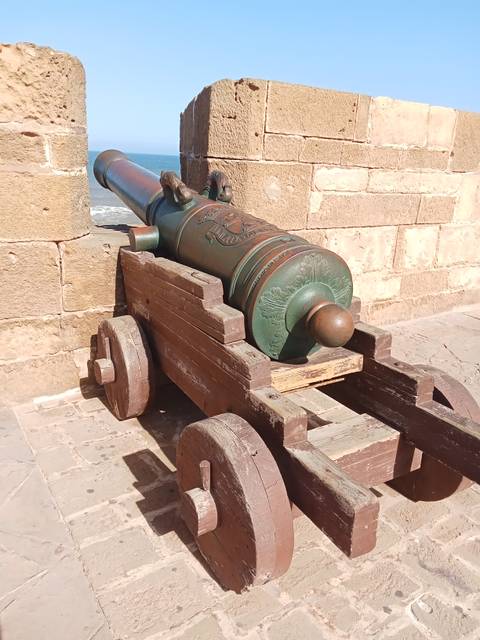 A historic cannon on a wooden carriage against a stone wall.