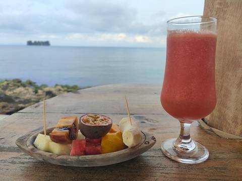       Plate of tropical fruits and a drink, with a lake view.
  