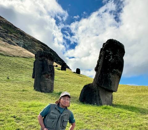 Person with Moai statues in a grassy field.