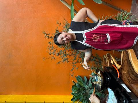 Person smiling while cooking outdoors with an orange wall.