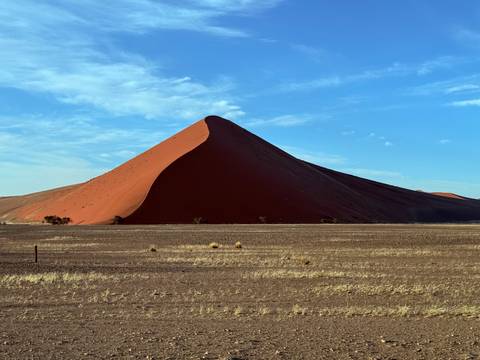       Red sand dune under a clear blue sky.
  