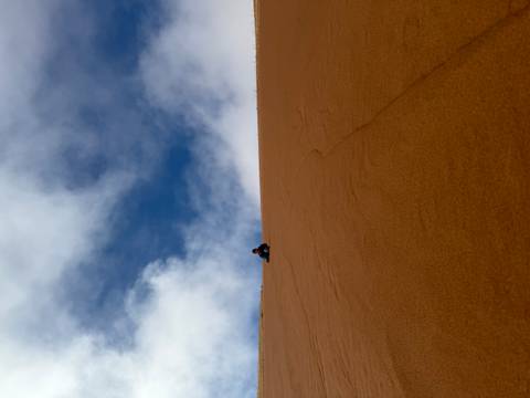       One person climbing a tall sand dune.
  