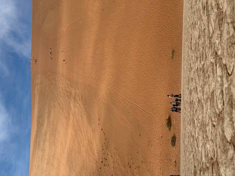 Group of people at the bottom of a large sand dune.