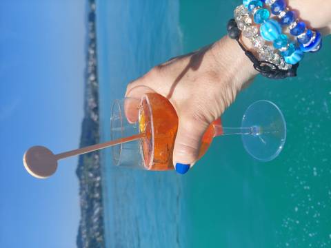 A hand holding an orange drink with a view of a blue lake.
