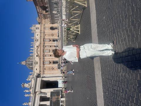 Man in white clothing standing in front of a large building with a dome.