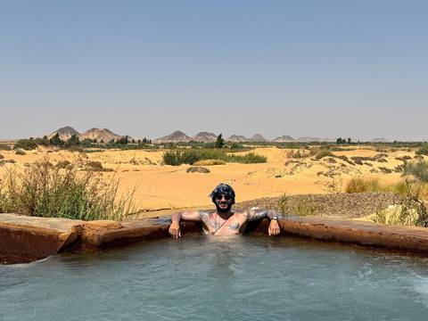 Person relaxing in a hot spring in a desert landscape.