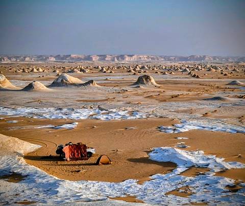 Vast desert landscape with unique rock formations and a vehicle.