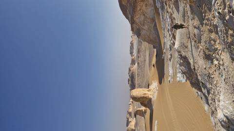 Person walking along a rocky desert landscape under a bright blue sky.