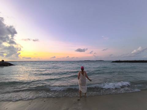 Person standing at the water's edge during a colorful sunset.