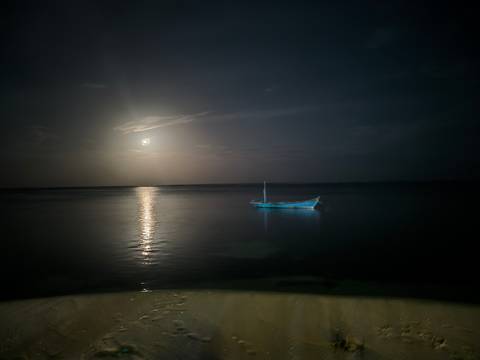 Moonlit night scene with a boat floating in the calm sea.