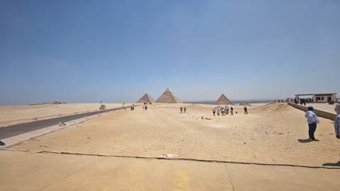 Panoramic view of the Pyramids of Giza with tourists in the foreground under a clear blue sky.